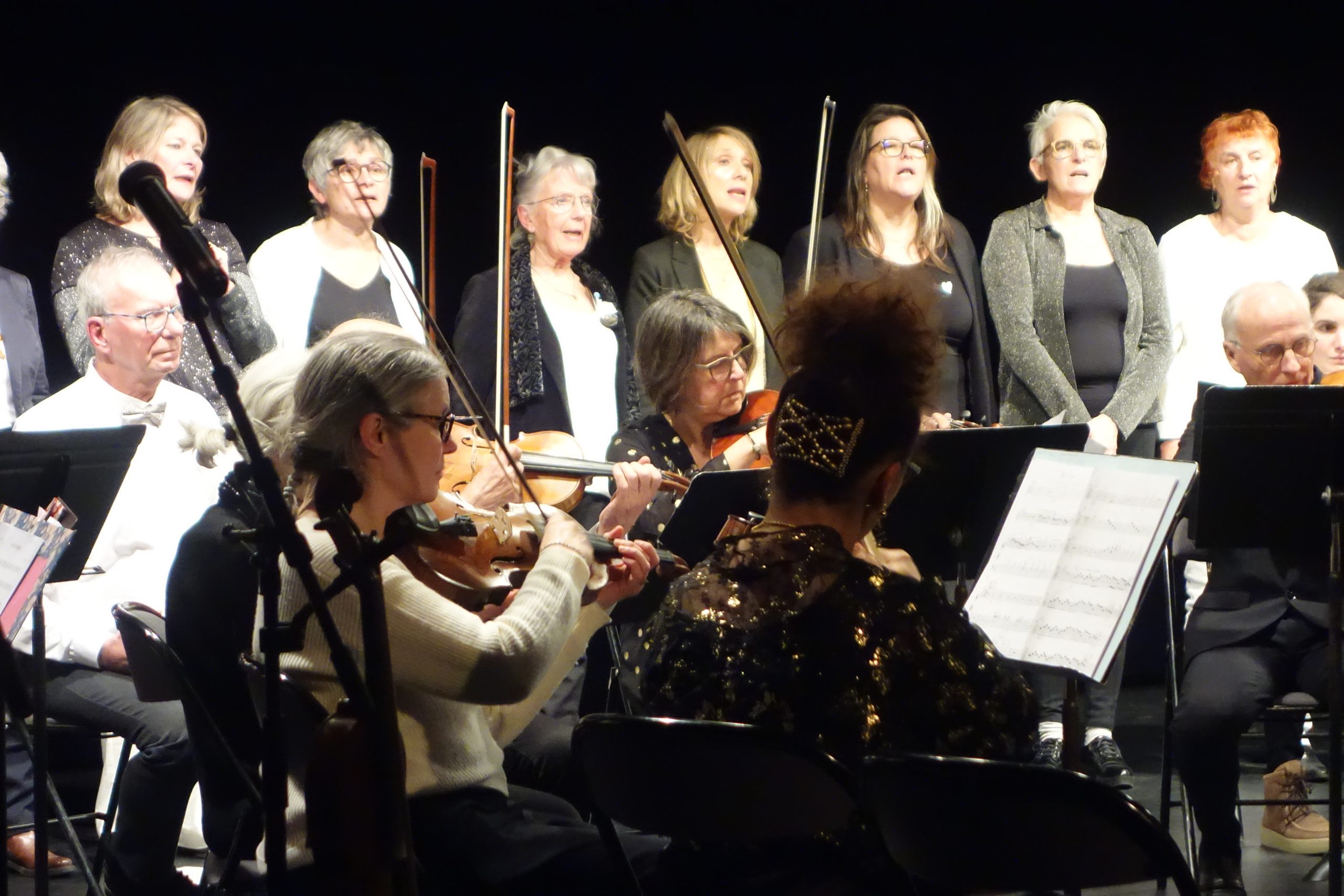 Au premier plan, des violonistes et altistes assis et à l'arrière plan, des choristes debout.