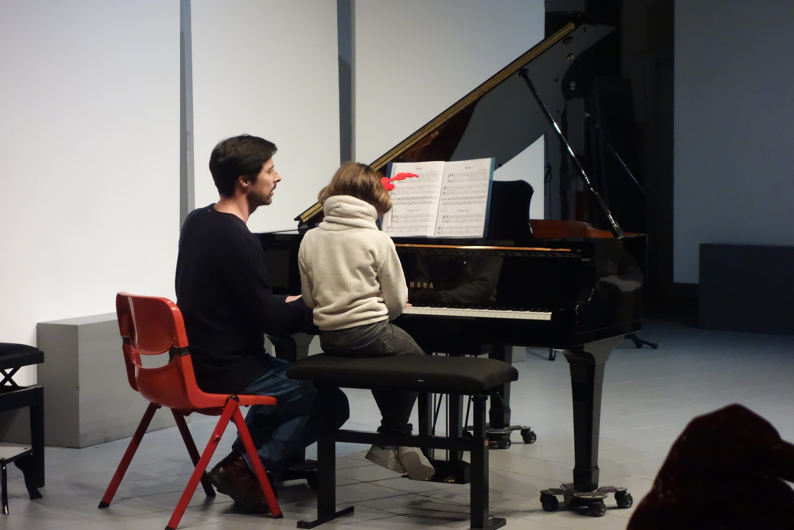 Une petite élève pianiste et son professeur assis devant un piano à queue.