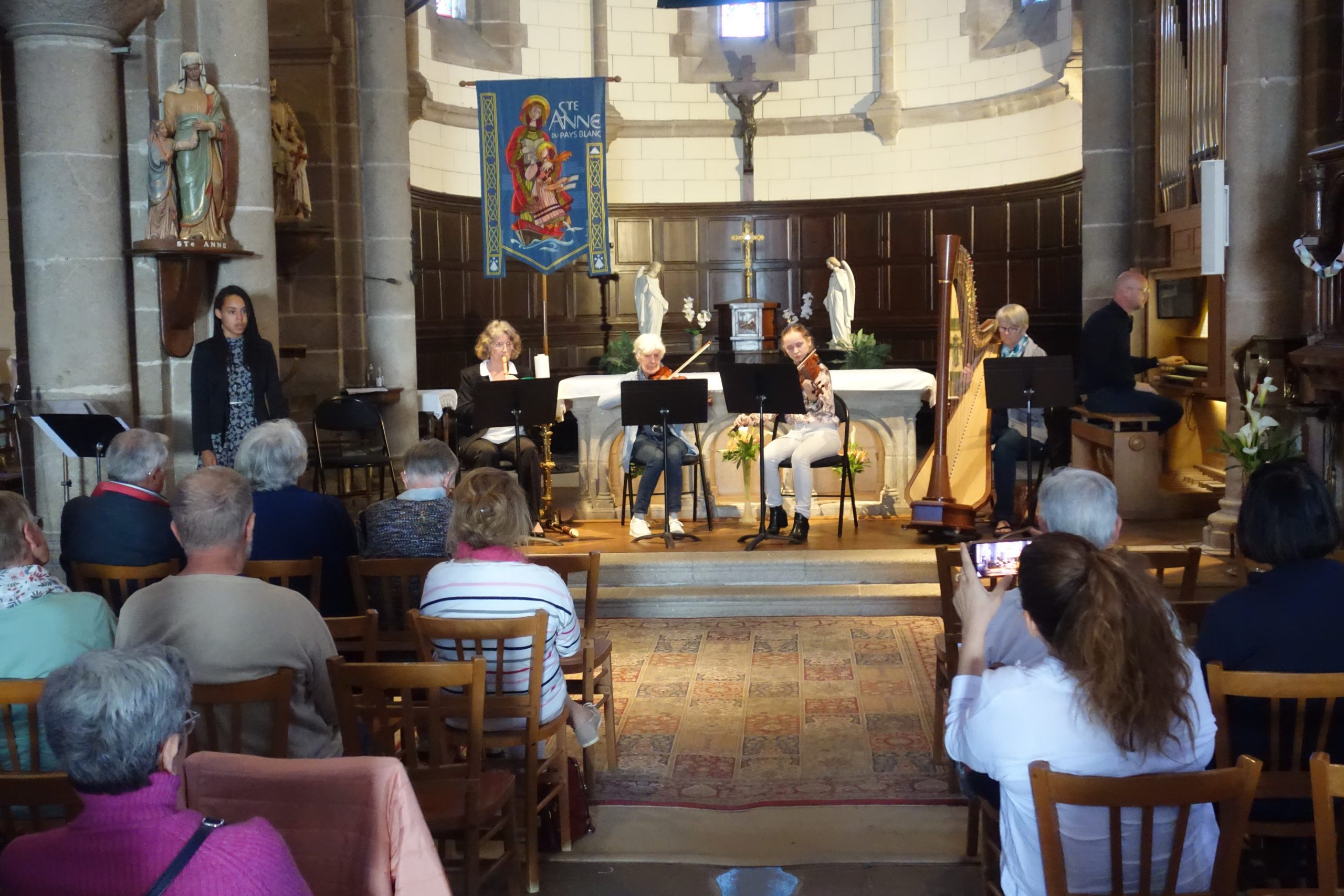 4 musiciennes de l'ensemble baroque sur scène (2 violonistes, 1 harpiste et 1 flûtiste) accompagnées à l'orgue par leur enseignant Christophe Gauche et une jeune chanteuse soliste devant un public dans l'église de Trescalan à La Turballe.