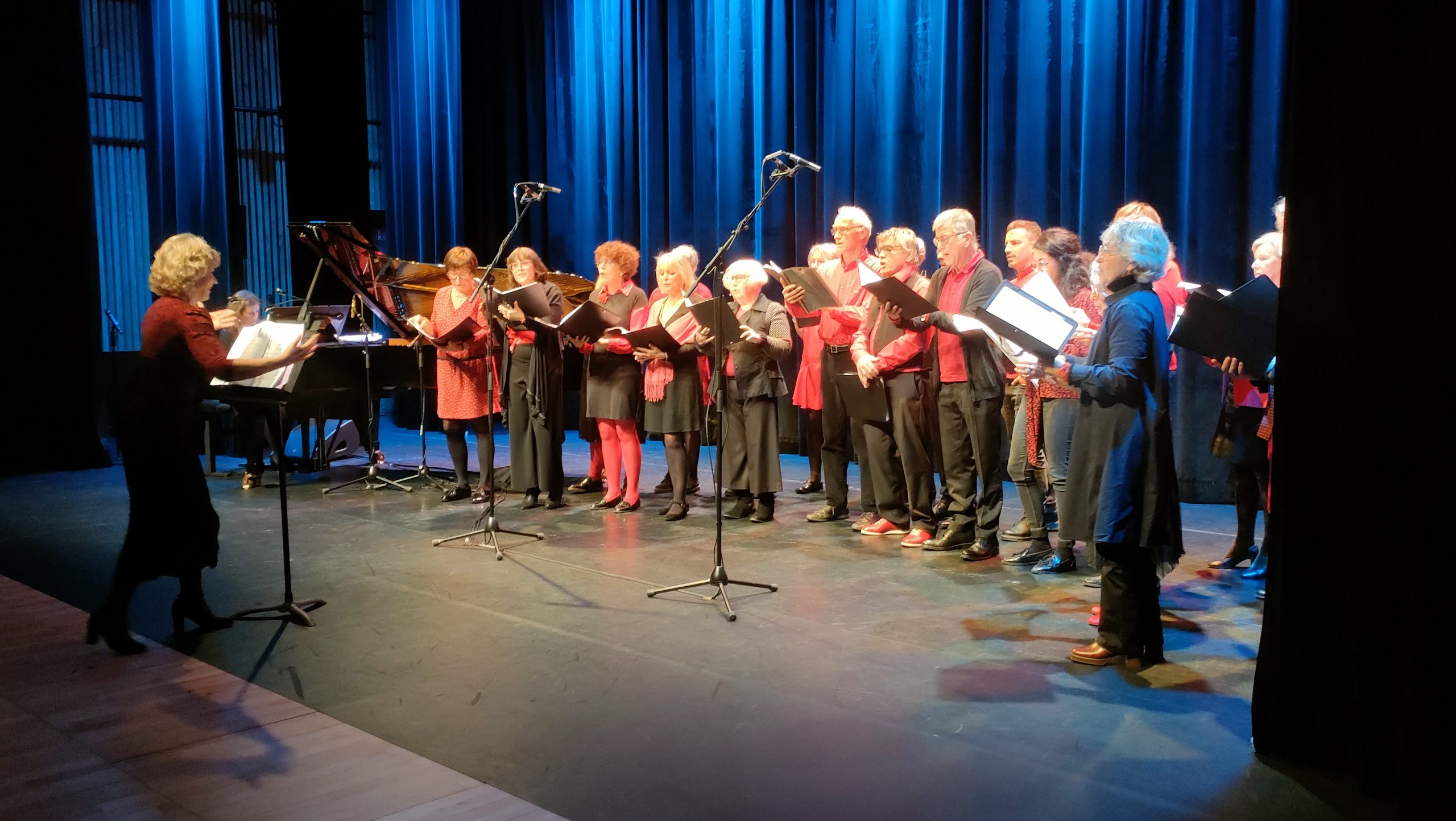 L'ensemble vocal adulte en train de chanter sur scène à côté d'un piano à queue sous la direction de Françoise Lemée.